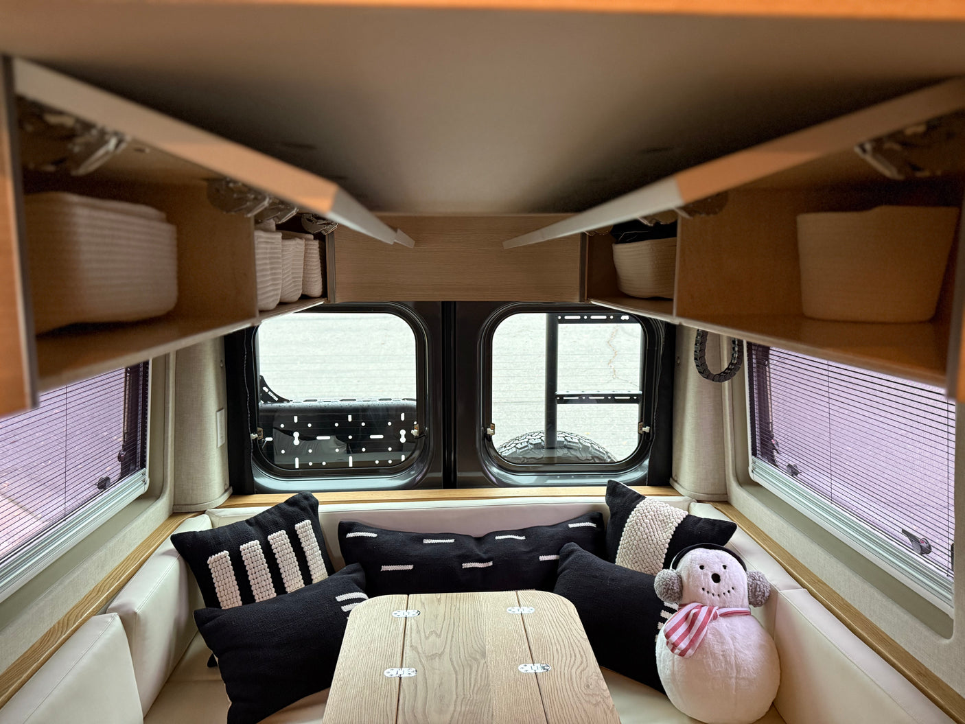Cozy rv rental interior featuring white seating, black/white pillows, overhead storage, and a central table, ready for adventures.