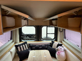 Cozy rv rental interior featuring white seating, black/white pillows, overhead storage, and a central table, ready for adventures.