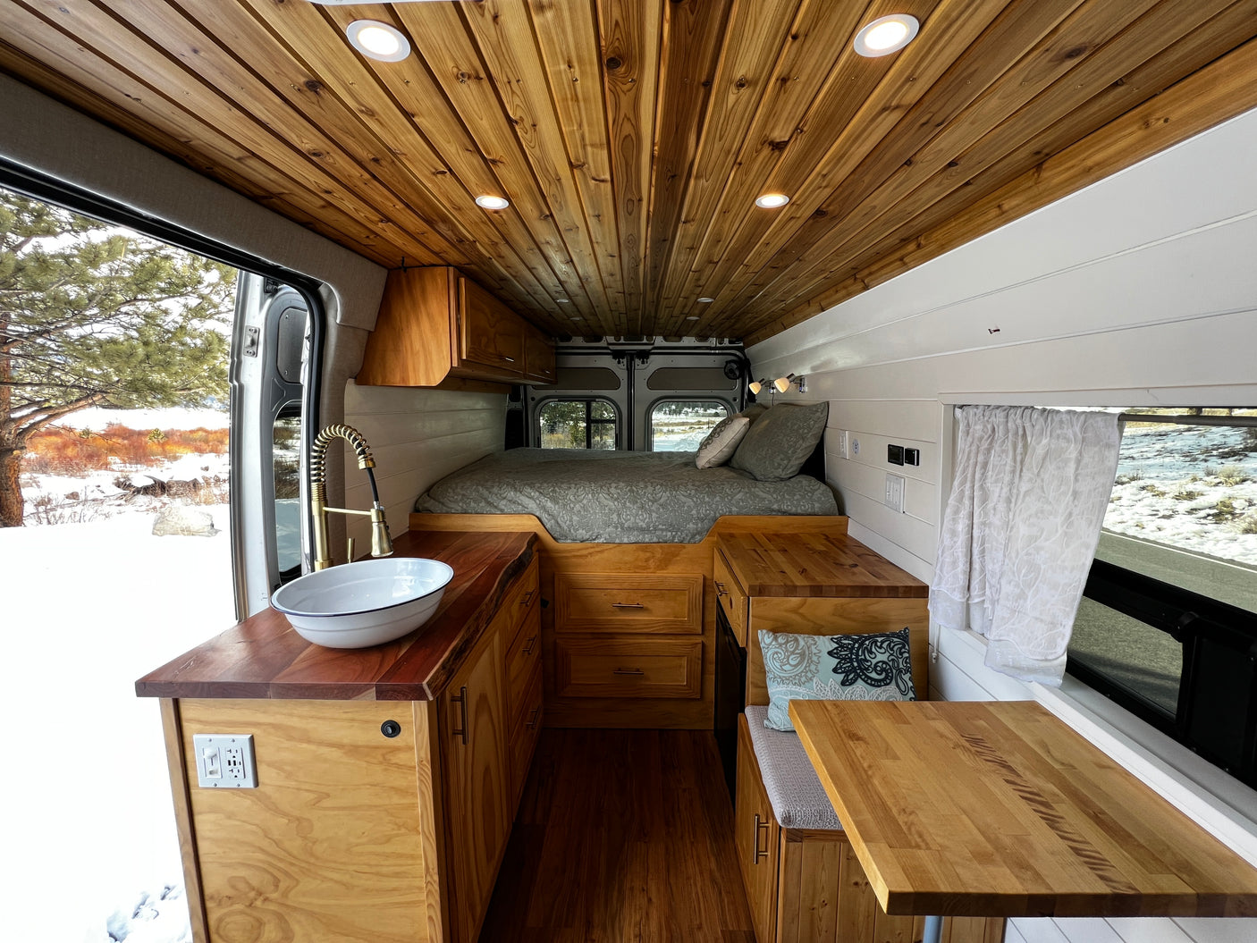 Inviting RV rental camper van interior with warm wood, cozy bed, kitchenette, and dinette, ideal for a snowy escape.