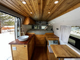 Inviting RV rental camper van interior with warm wood, cozy bed, kitchenette, and dinette, ideal for a snowy escape.