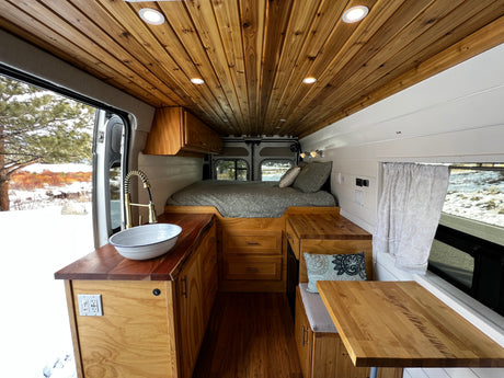 Inviting RV rental camper van interior with warm wood, cozy bed, kitchenette, and dinette, ideal for a snowy escape.