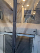 View of a comfortable RV rental interior through a mesh screen, featuring seating/bedding and bright overhead lighting.