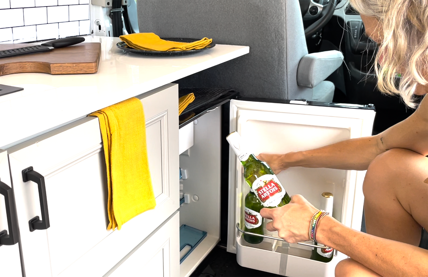 Grabbing cold Stella Artois from the RV rental fridge. Perfect for relaxing in this compact camper kitchen setup.