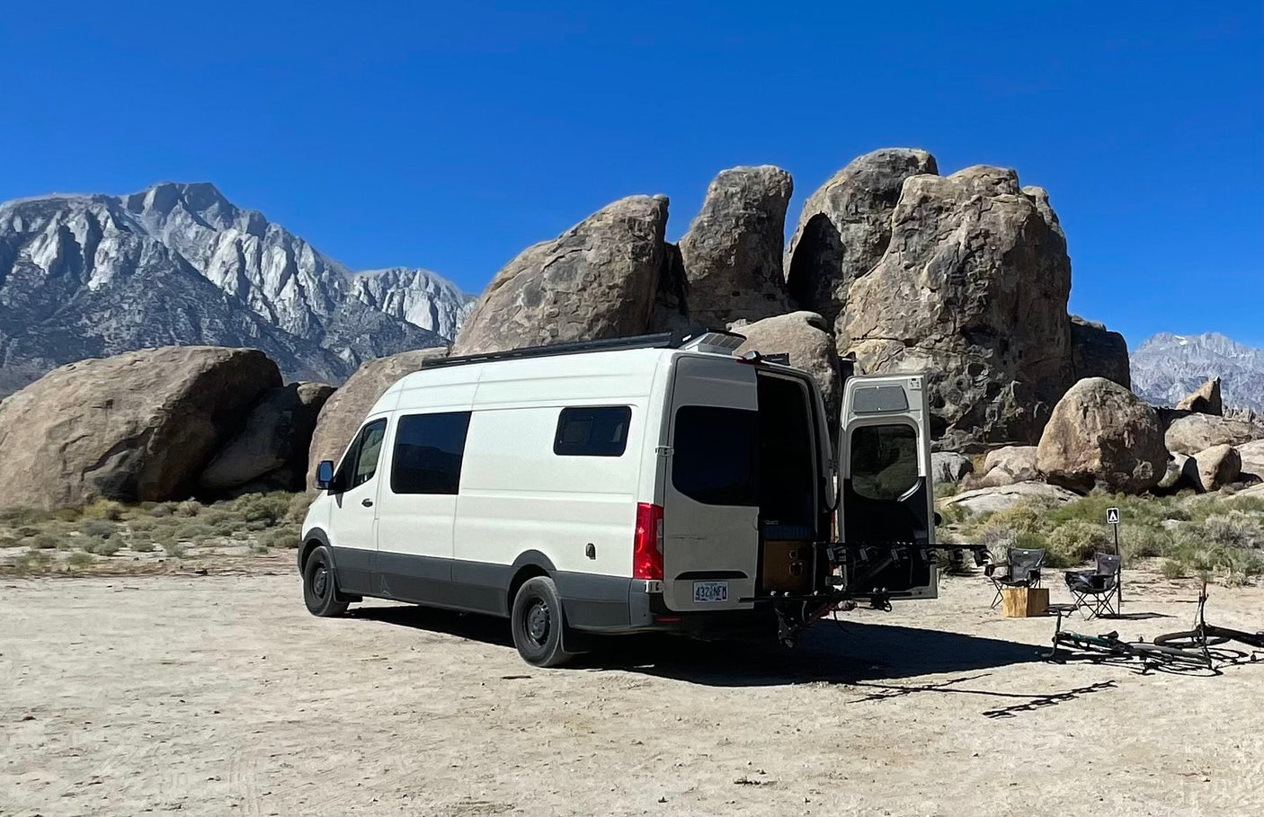 Enjoy the outdoors in an rv rental! White camper van parked by massive boulders, stunning mountains, bikes & camp setup.