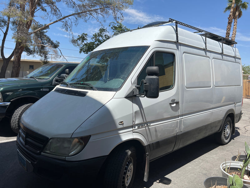 Front-left view of a white Mercedes Sprinter van with a roof rack, likely an RV rental. A green F250 truck is parked next to it. — photo 8