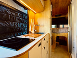 Explore this efficient RV rental with a modern kitchen, induction stove, sink, and comfy raised bed in warm wood tones.