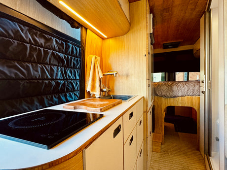 Explore this efficient RV rental with a modern kitchen, induction stove, sink, and comfy raised bed in warm wood tones.