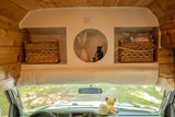 Inside a well-organized RV rental: custom overhead storage with woven baskets, decorative items, and a plush trim.