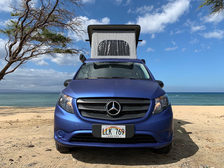Hawaii RV rental: Blue Mercedes-Benz camper van with pop-top open on a sunny sandy beach by the ocean.