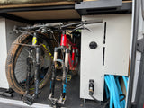 RV rental with muddy mountain bikes securely stored inside, featuring a utility panel with a hose for post-ride cleanup.