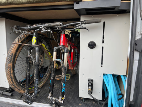 RV rental with muddy mountain bikes securely stored inside, featuring a utility panel with a hose for post-ride cleanup.