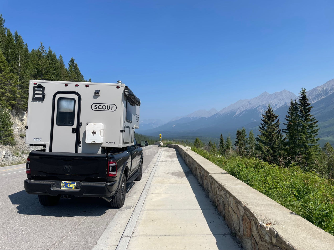 Scout Olympic truck camper, an RV rental option, parked on a mountain road with clear skies and distant peaks. — photo 8