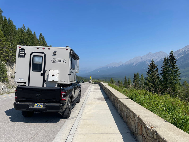 Scout Olympic truck camper, an RV rental option, parked on a mountain road with clear skies and distant peaks. — photo 8