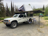 Overland camping setup: white pickup truck with rooftop tent & awning. Ideal for your next RV rental trip!