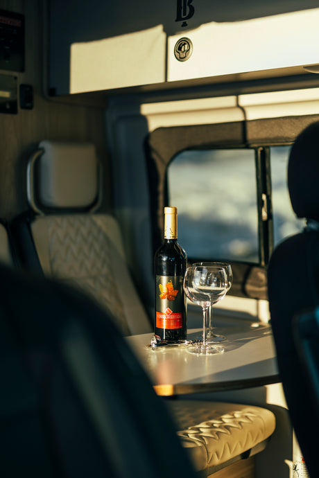 Relax with a bottle of wine and glasses on the table inside this cozy RV rental, ideal for a peaceful getaway.