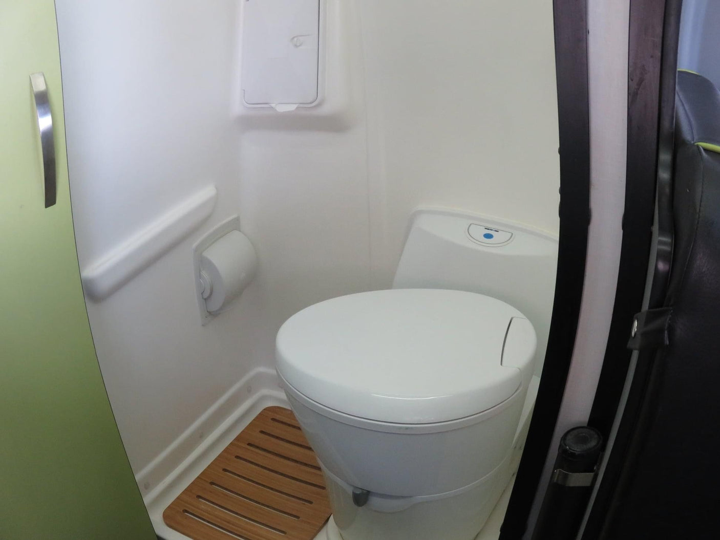 Compact RV rental bathroom with white toilet, integrated shower, and wooden floor mat for efficiency.