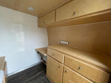 This RV rental interior features light wood cabinetry, a power strip, and functional storage, ideal for a comfortable camper setup.
