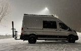 Snow-covered rv rental: White camper van with skis on back in heavy snowfall. Ideal for winter adventures.