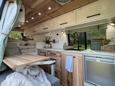 Cozy RV rental interior, featuring a well-equipped kitchen, wooden accents, and a clever Lagun table setup. Perfect home on wheels.