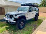 White Jeep Wrangler Rubicon with a roof tent, ready for adventure. Explore the outdoors with this unique RV rental.