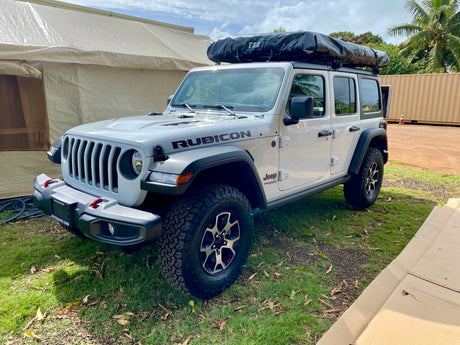 White Jeep Wrangler Rubicon with a roof tent, ready for adventure. Explore the outdoors with this unique RV rental.