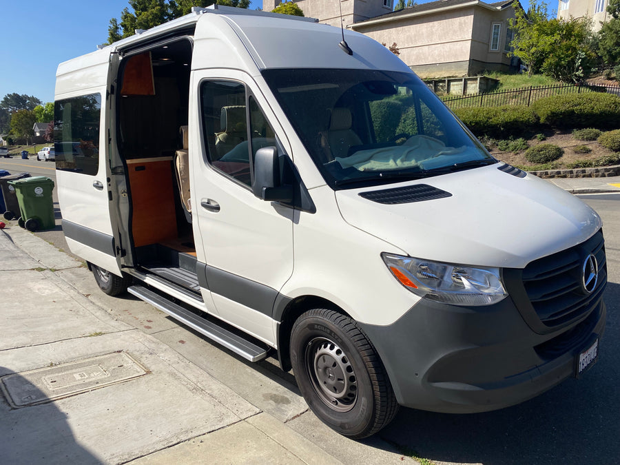 White Mercedes-Benz Sprinter camper van, ideal for rv rental, with its side door open showing a custom wood interior.