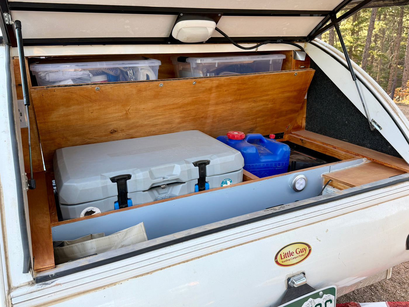 An rv rental teardrop camper's open galley features a cooler, water jugs, and clear bins, neatly organized for travel. — photo 12