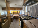RV rental interior features a compact kitchen with stove, dining table, and cozy bench seating that converts to a bed.