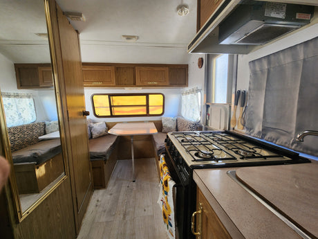 RV rental interior features a compact kitchen with stove, dining table, and cozy bench seating that converts to a bed.