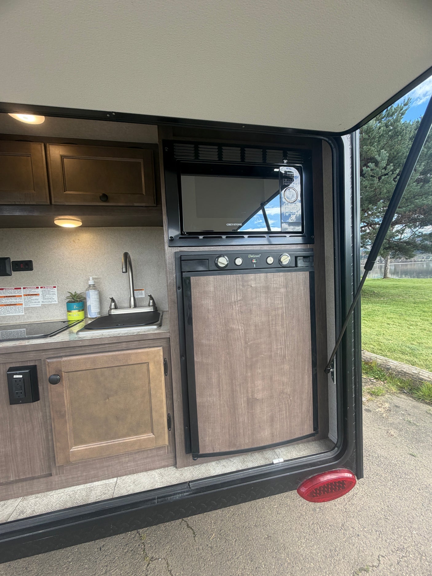 RV rental outdoor kitchen: microwave, fridge, and sink, overlooking a lake. Ready for your next camping adventure!