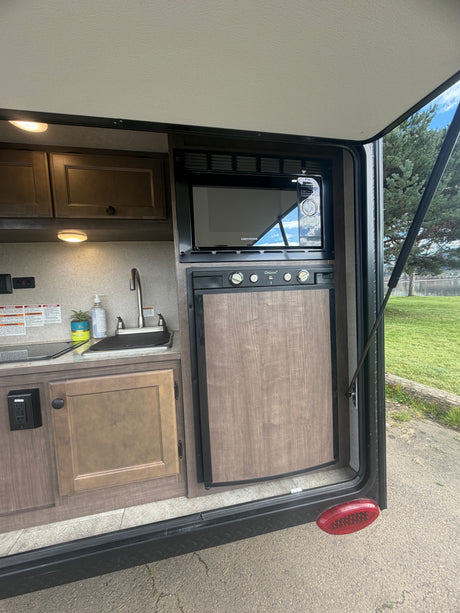 RV rental outdoor kitchen: microwave, fridge, and sink, overlooking a lake. Ready for your next camping adventure!