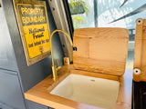 RV rental's clever kitchen setup: Kohler sink, brass faucet, wood counters, and a unique National Forest sign.