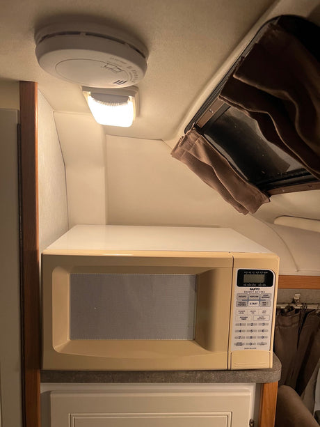 View inside an RV rental showing a Sanyo microwave, a smoke detector on the ceiling, and an overhead light.