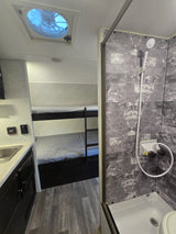 This rv rental features a compact interior with bunk beds, a kitchen sink, and a tiled shower, plus a ceiling fan.