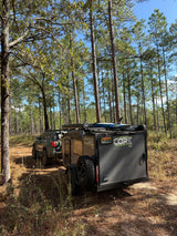 Off-road rv rental adventure: SUV towing a CORE RV trailer with a dog through a serene pine forest.