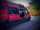Open door on a vibrant red RV rental van, showcasing its spacious interior on a fall day. Ready for adventure!