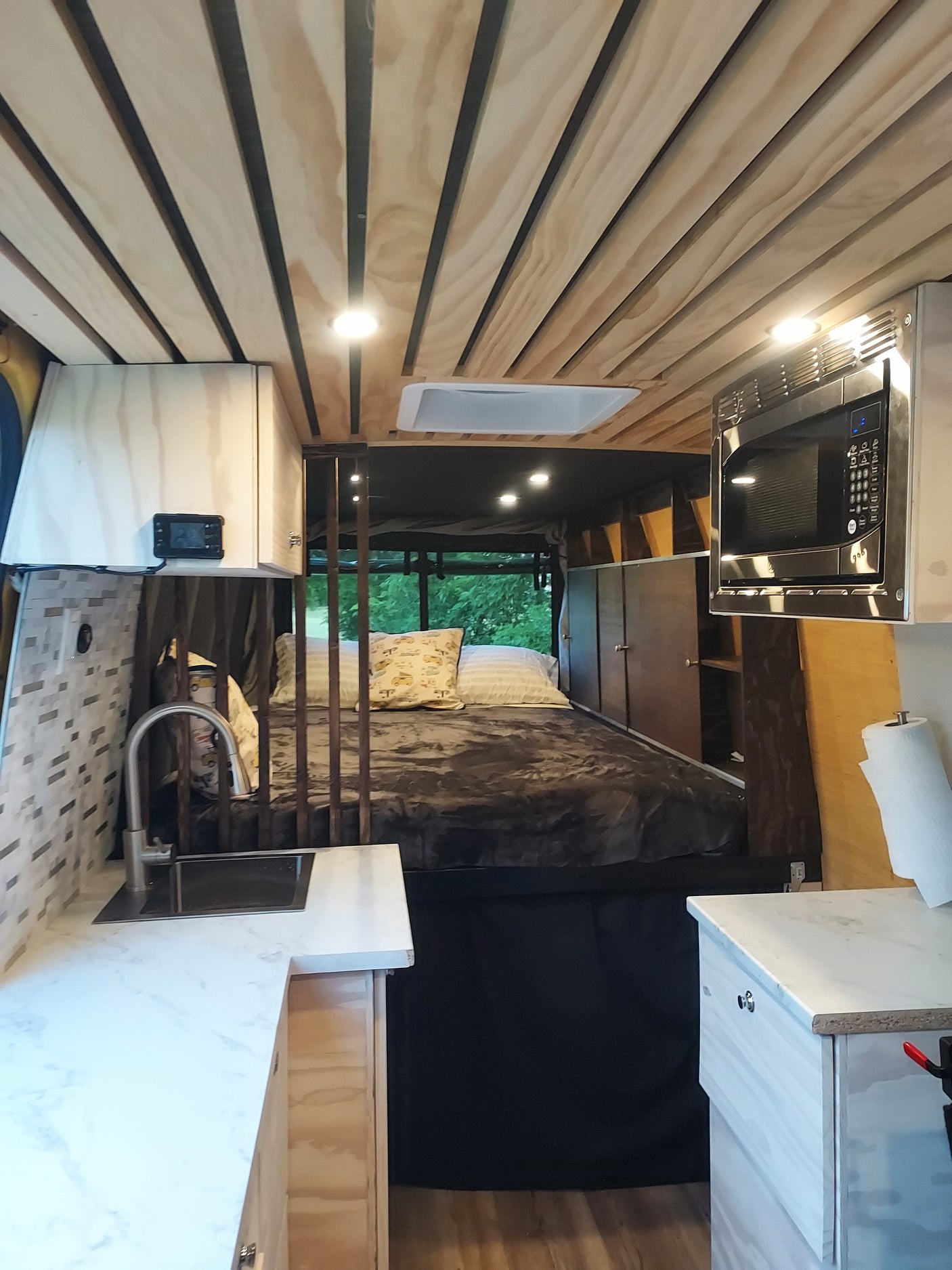 Cozy RV rental interior featuring a compact kitchen with microwave and sink, and a comfortable bed area.