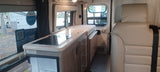 RV rental camper van interior featuring a compact kitchen with a stovetop, sink, fridge, and comfortable seating.