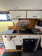 RV rental kitchen: modern sink, stove, and smart storage like a knife rack & cutting board in a camper van.
