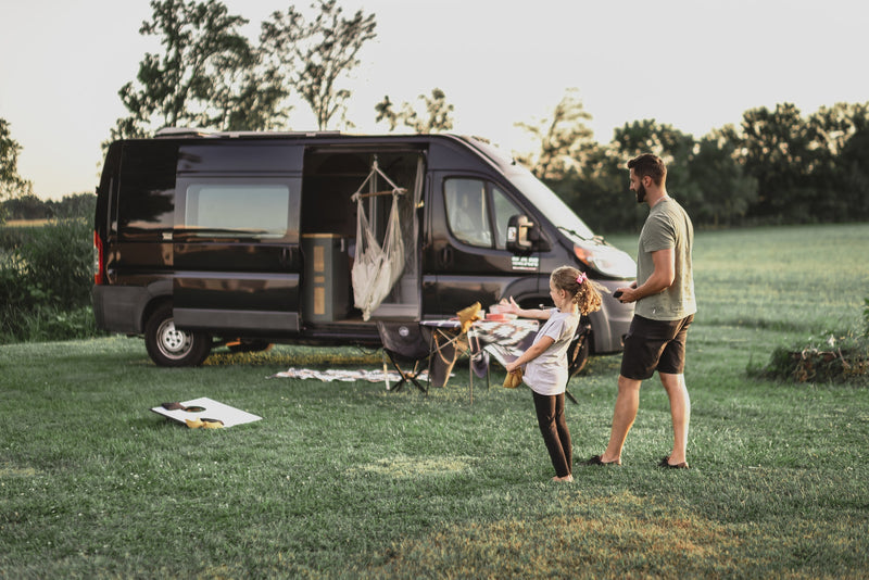 RV rental family fun: A dad and daughter play games in a grassy field next to their open camper van and camp setup. — photo 1