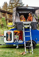 Family on an RV rental trip: parents relax in a rooftop tent, while kids read inside the blue camper.