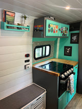 RV rental kitchen: Compact, mint-accented interior with stove, wooden counter, bench, & unique decor. Ideal for van life.