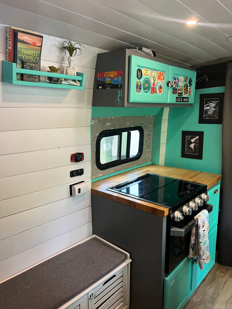 RV rental kitchen: Compact, mint-accented interior with stove, wooden counter, bench, & unique decor. Ideal for van life.