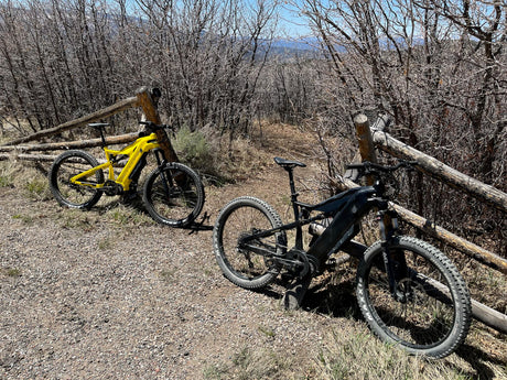 Two e-bikes on a mountain trail beside a rustic fence. Your RV rental can lead to scenic outdoor adventures like this!