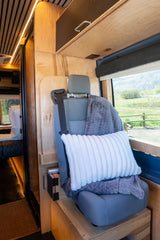 Comfortable RV rental interior: cozy seat with pillow and blanket, warm wood paneling, LED lighting, and a scenic window view.