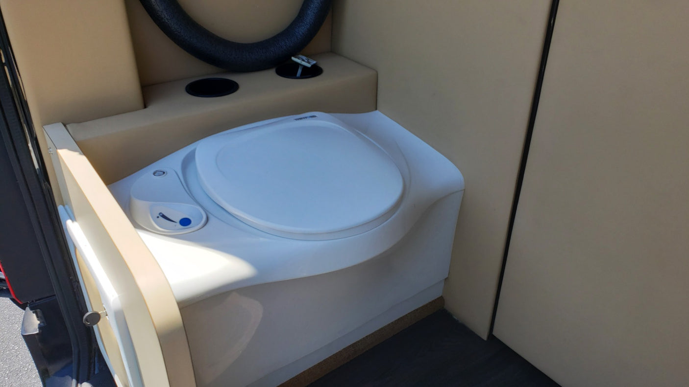 Inside an RV rental: a clean, compact toilet with beige interior. Essential for comfortable travel.