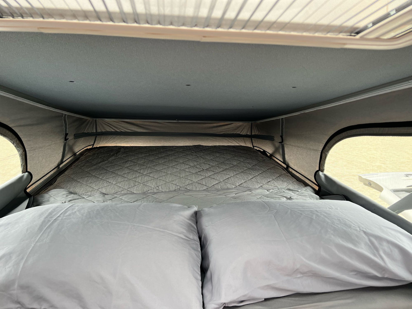 Cozy bed inside an RV rental pop-top camper, featuring two pillows and a quilted mattress for a comfortable sleeping area. — photo 16