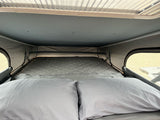 Cozy bed inside an RV rental pop-top camper, featuring two pillows and a quilted mattress for a comfortable sleeping area.