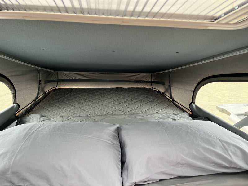 Cozy bed inside an RV rental pop-top camper, featuring two pillows and a quilted mattress for a comfortable sleeping area. — photo 16