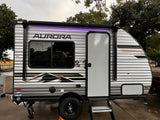 This Aurora travel trailer RV rental, with its illuminated awning and side door, is set up for a comfortable outdoor adventure.